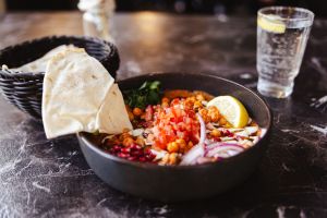 Schale mit Hummus, Kichererbsen, Tomatenwürfeln und Fladenbrot