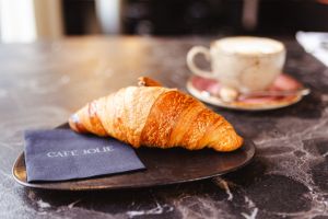Croissant auf einem Teller, im Hintergrund eine Kaffeetasse