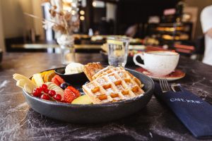 Waffeln mit Puderzucker und frischen Früchten, im Hintergrund eine Kaffeetasse