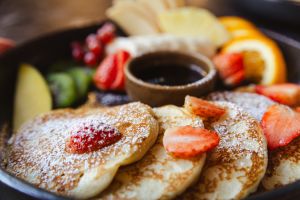 Pancakes mit Puderzucker, Erdbeeren, weiteren Früchten und Sirup