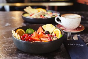 Schale mit Müsli und frischen Früchten, daneben eine Kaffeetasse