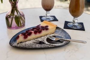 Ein Stück Beeren-Käsekuchen auf einem mit Puderzucker bestreuten Teller mit einer Kuchengabel daneben.